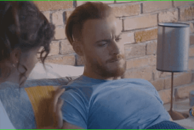a man in a blue shirt is laying on a couch with a woman