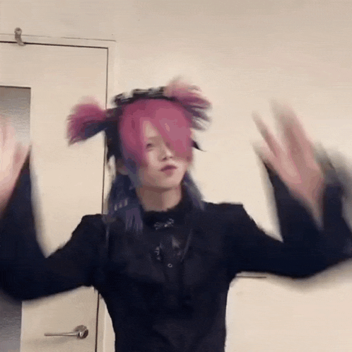 a person with pink hair and purple eyes is standing in front of a door with their arms outstretched .