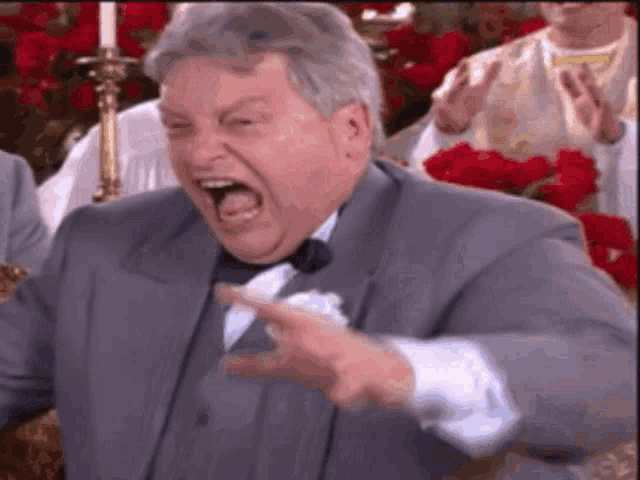 a man in a suit and bow tie is making a funny face and pointing .