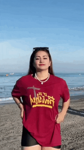 a woman is standing on a beach wearing a red t-shirt and black shorts .