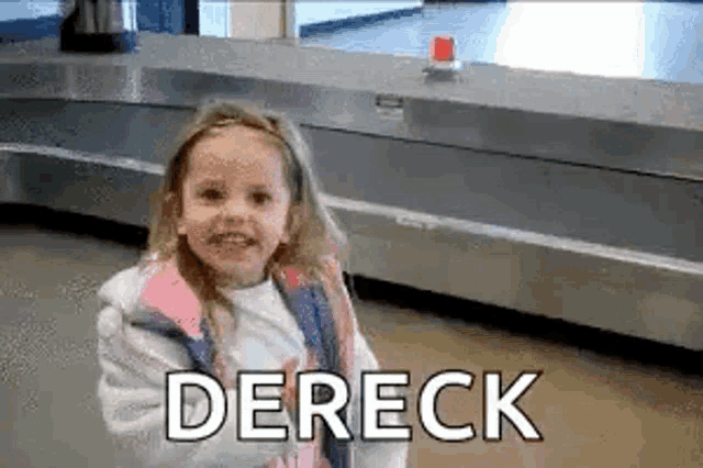 a little girl is standing in front of a conveyor belt at an airport and smiling .