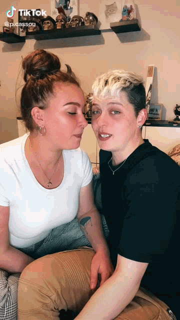 a woman is kissing another woman on the cheek while sitting on a bed .