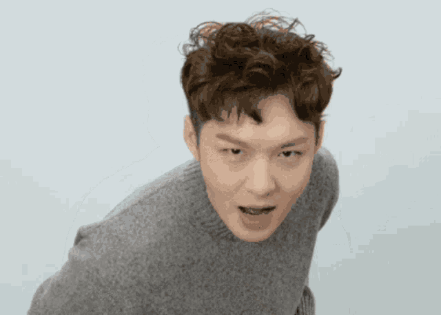 a man with curly hair wearing a grey sweater is making a funny face