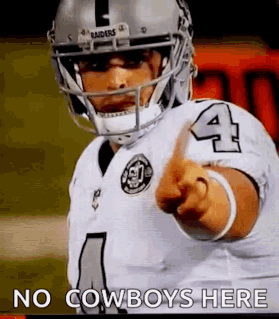 a football player wearing a helmet and pointing at the camera .