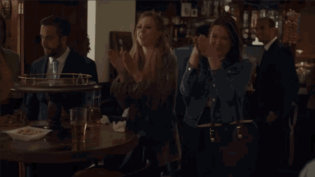 a group of people clapping in a bar with a man in a suit