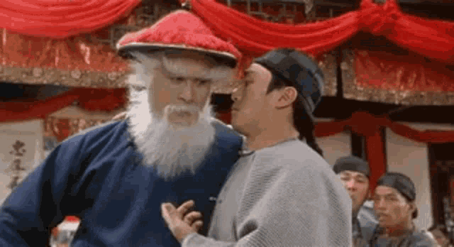 a group of men are standing next to each other in a room . one of the men is wearing a santa hat .