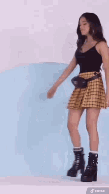 a woman wearing a plaid skirt and black boots is standing in front of a blue background .