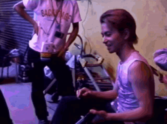 a man in a backstage shirt stands behind a man playing a drum set