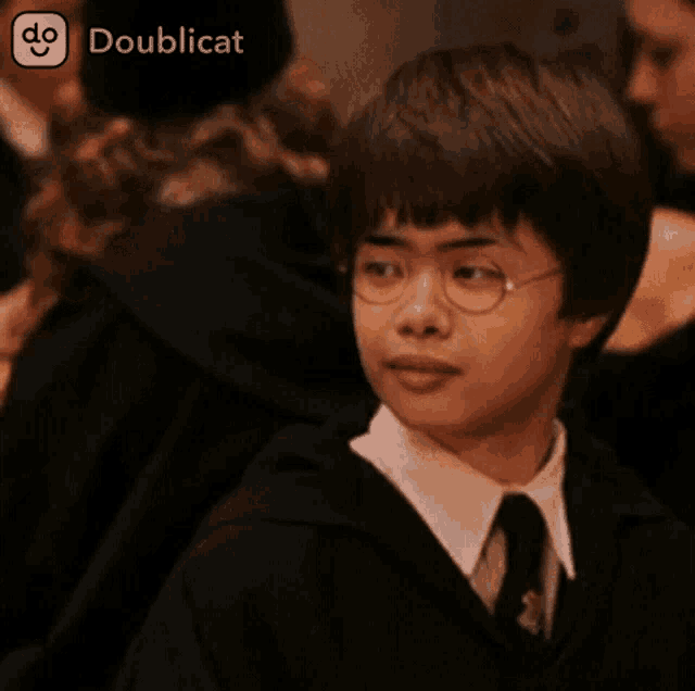 a young boy wearing glasses and a tie looks at the camera with a doublecat icon in the corner