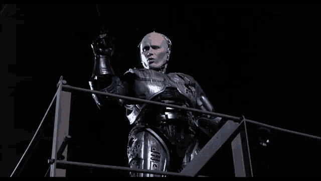 a man in a robotic suit is standing on a railing pointing