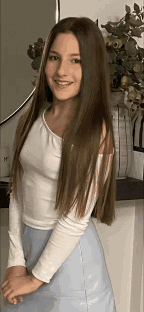 a girl with long brown hair wearing a white top and blue skirt