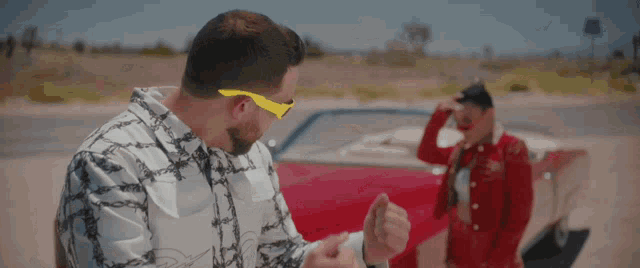 a man wearing yellow sunglasses stands next to a woman in a red dress
