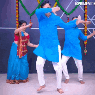 a man in a blue shirt is dancing with two other men in white pants