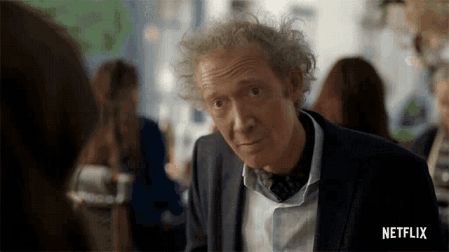 a man with curly hair in a suit and tie is talking to a woman in a restaurant .