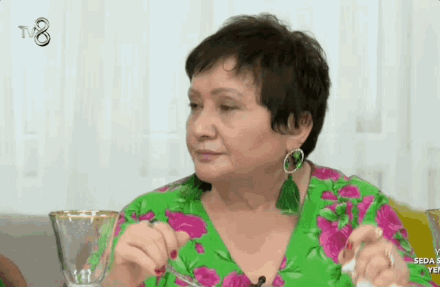 a woman in a green and pink floral shirt holds a glass in front of a tv8 logo