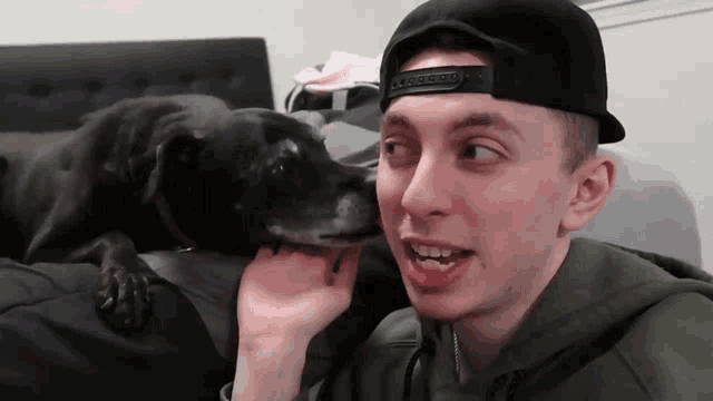 a man wearing a black hat and a green hoodie is petting a black dog