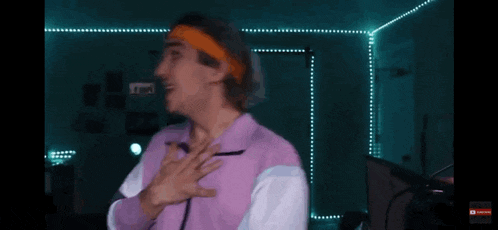a man wearing a headband and a purple jacket has his hands on his head in front of a sign that says subscribe
