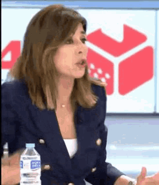 a woman in a blue jacket is holding a bottle of water and talking .