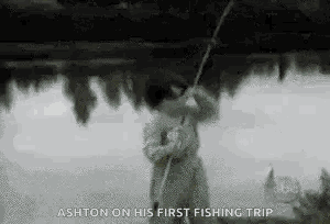 a black and white photo of a man holding a fishing rod in front of a body of water .