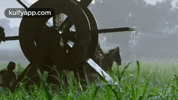 a group of people are riding horses in a field with a water wheel in the foreground .