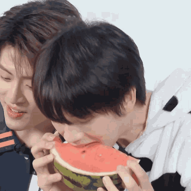 a man is eating a slice of watermelon while another man looks on