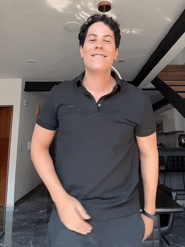 a man wearing a black polo shirt is smiling in a room