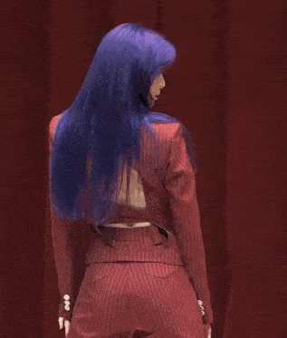 a woman with purple hair is wearing a red suit with a back cut out .