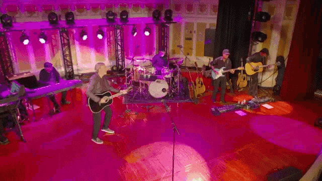 a group of people playing instruments on a stage with purple lights behind them