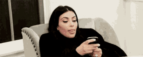 kim kardashian is sitting in a chair looking at her phone .