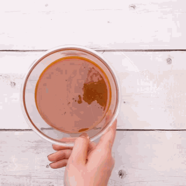 a person is holding a bowl of sauce on a wooden table