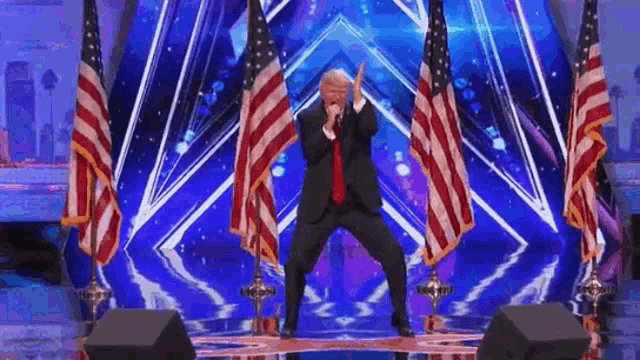 a man in a suit and tie is standing on a stage in front of american flags .
