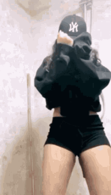a woman wearing a ny hat and shorts is standing in a shower .