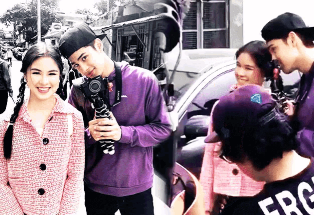 a man in a purple shirt is holding a camera while a woman in a pink jacket looks on