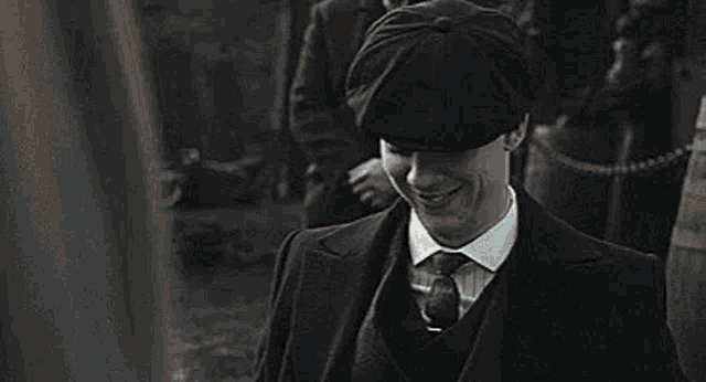 a man in a suit and tie is wearing a flat cap .