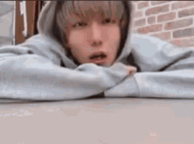 a man in a hoodie is laying on a table with his head on his arms .