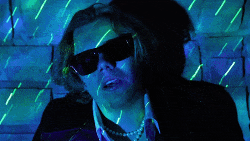 a man wearing sunglasses and a pearl necklace is surrounded by glowing lights