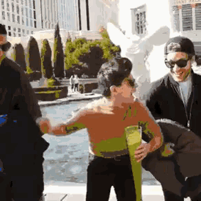 a group of people are standing around a pool with a statue in the background and one of them is wearing sunglasses