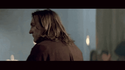 a man with long hair is standing in front of a blue wall