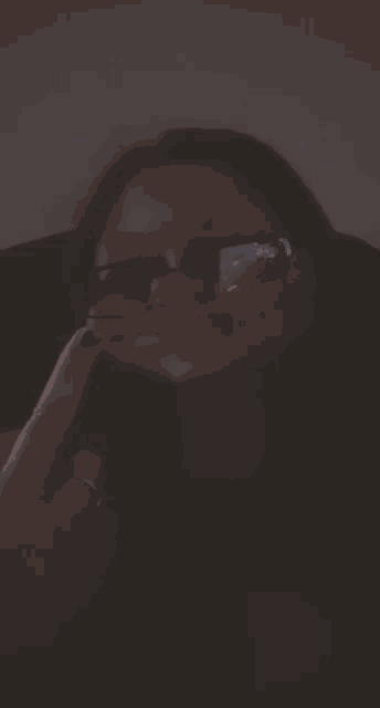 a woman wearing sunglasses and a black shirt is covering her mouth with her hand .