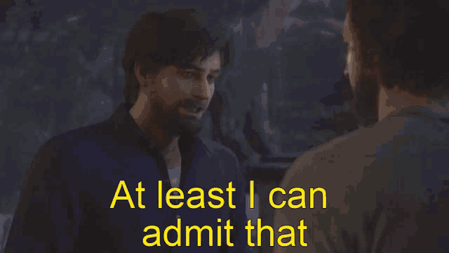 a man with a beard is talking to another man with at least i can admit that written in yellow