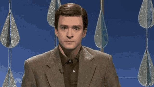 a man in a suit and polo shirt is standing in front of a blue background with hanging decorations .