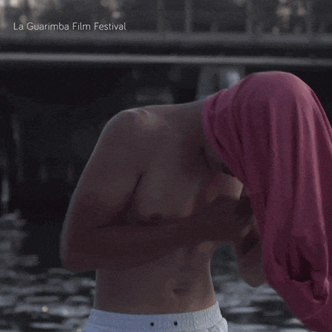 a shirtless man holding a pink shirt over his head with la guarimba film festival written on the bottom