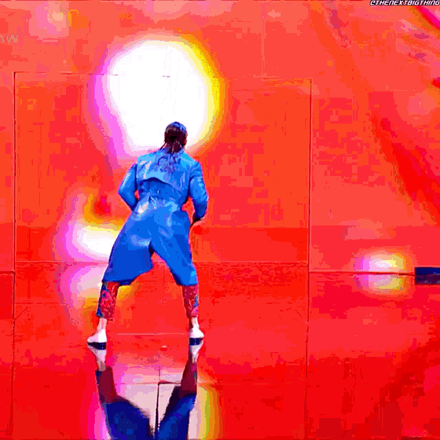 a woman in a blue trench coat is dancing on a stage