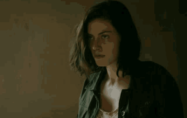 a woman in a black jacket looks at the camera with a serious look on her face