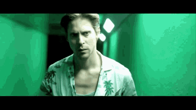 a man in a hawaiian shirt is walking down a hallway with a green background .