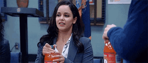 a woman in a suit is holding a bottle of orange juice in her hands .