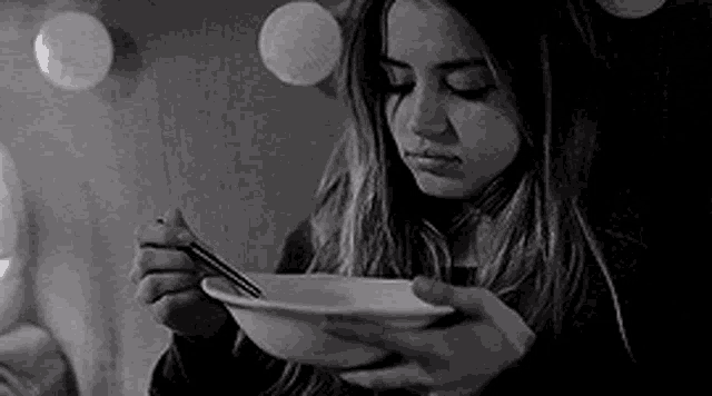 a woman is eating soup with chopsticks from a bowl .