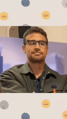 a man wearing glasses and a jacket stands in front of smiley faces
