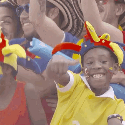 a young boy wearing a yellow shirt and a jester hat points to the camera