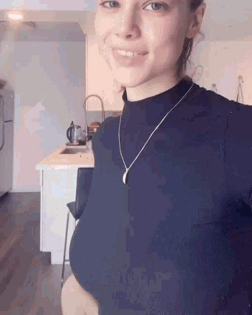 a woman wearing a black top and a silver necklace is smiling in a kitchen .